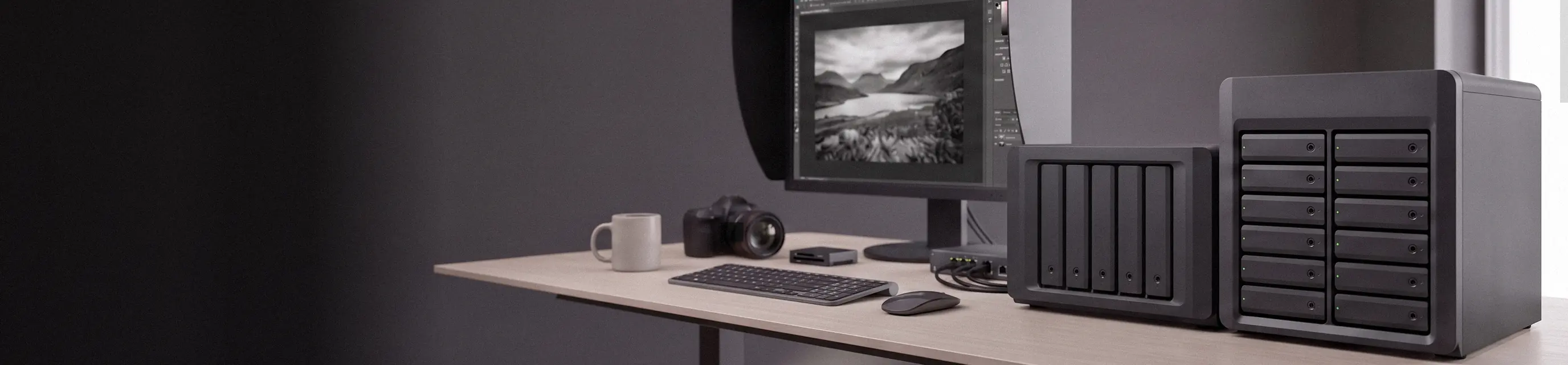 Postazione di un fotografo con due NAS in primo piano, monitor con paraluce e fotocamera
