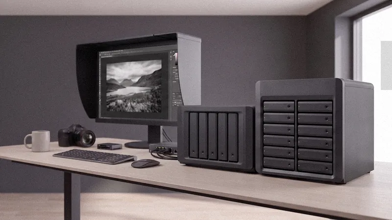Postazione di un fotografo con due NAS in primo piano, monitor con paraluce e fotocamera